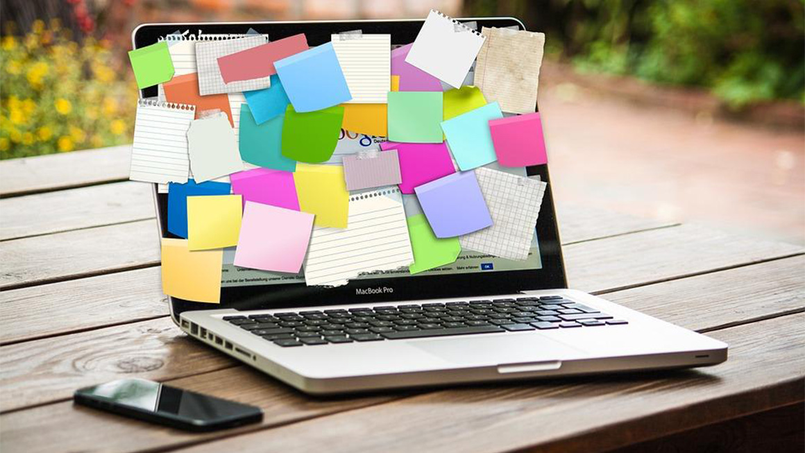 notebook sobre um tablado de madeira, com vários post its grudados na tela e um celular ao lado.