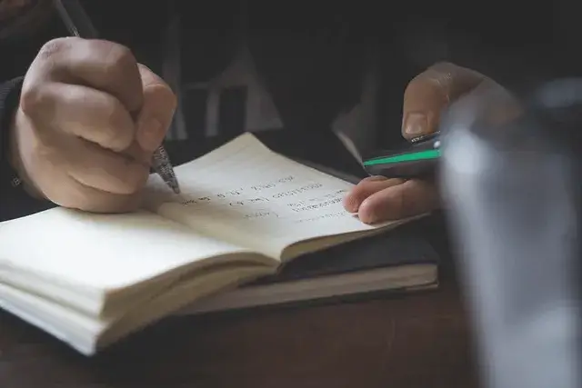 mãos escrevendo em um caderno de anotações.