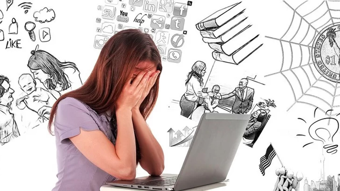 Mulher sentada na frente do computador, com as mãos no rosto.
