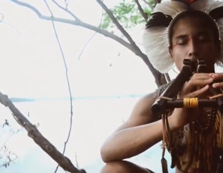 Flautista indígena sentado, tocando flauta.