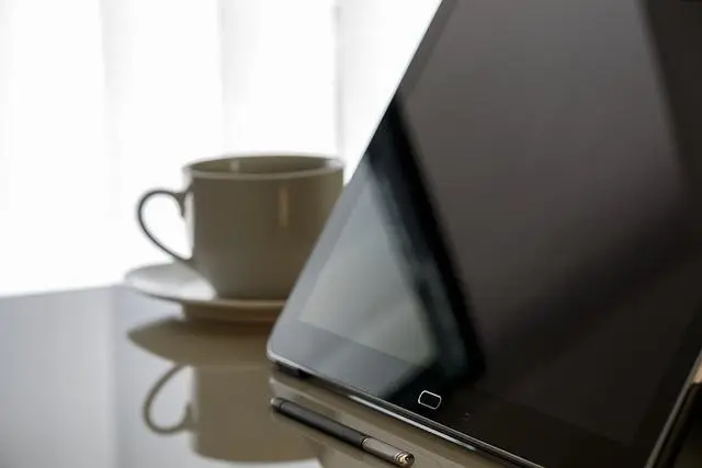 tablet ao lado de xícara de café